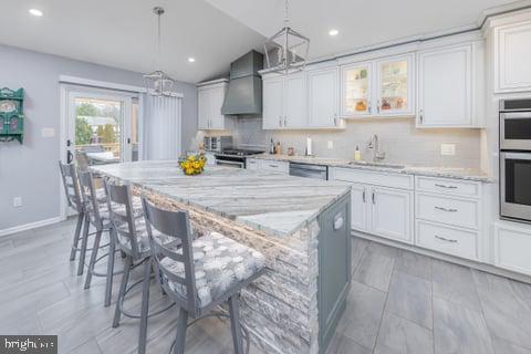 kitchen with a center island, wall chimney range hood, sink, and white cabinetry