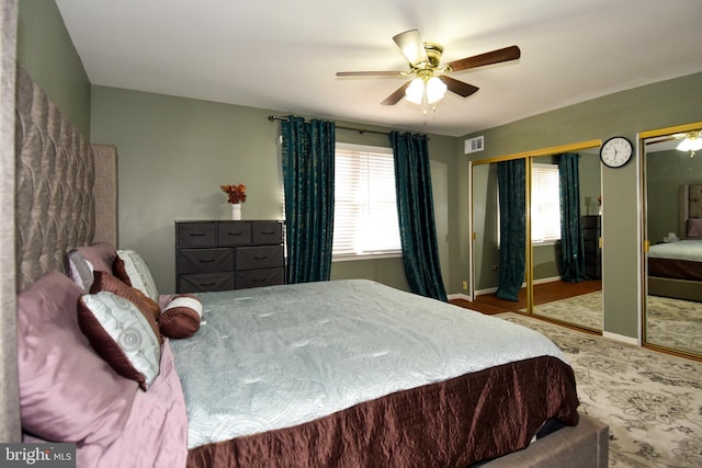 bedroom with multiple windows, two closets, and ceiling fan