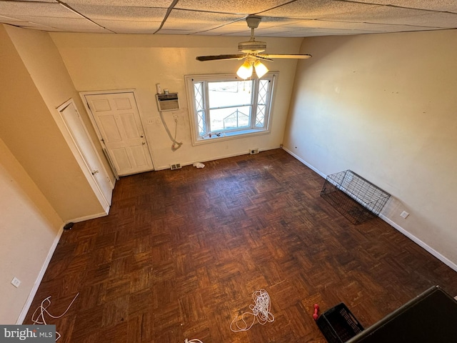 unfurnished dining area featuring ceiling fan, a drop ceiling, dark parquet flooring, and an AC wall unit