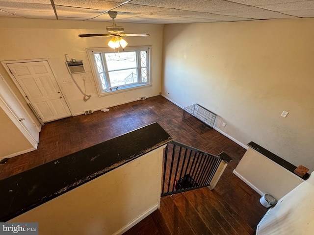 stairway with a wall mounted air conditioner, a drop ceiling, and ceiling fan