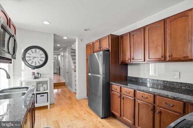 kitchen featuring appliances with stainless steel finishes, light hardwood / wood-style floors, dark stone countertops, and sink