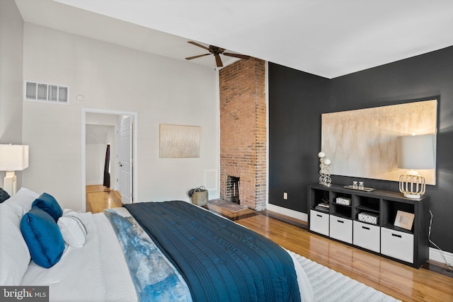 bedroom featuring ceiling fan, a fireplace, and wood-type flooring