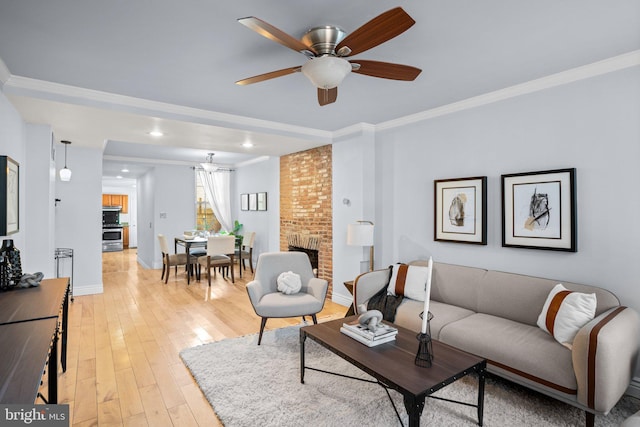 living room featuring a brick fireplace, light wood-type flooring, ceiling fan, and crown molding