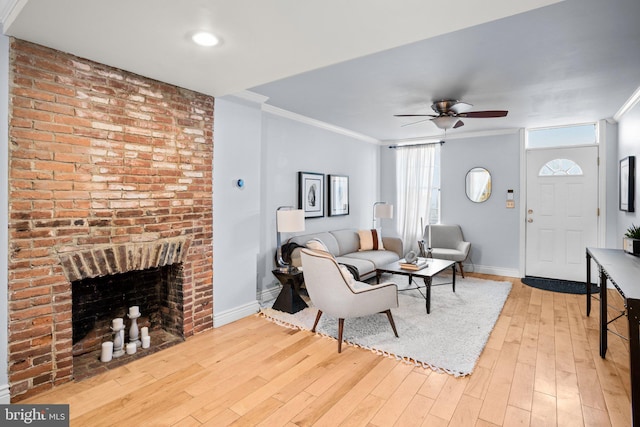 living room featuring a fireplace, light wood-type flooring, ceiling fan, and ornamental molding