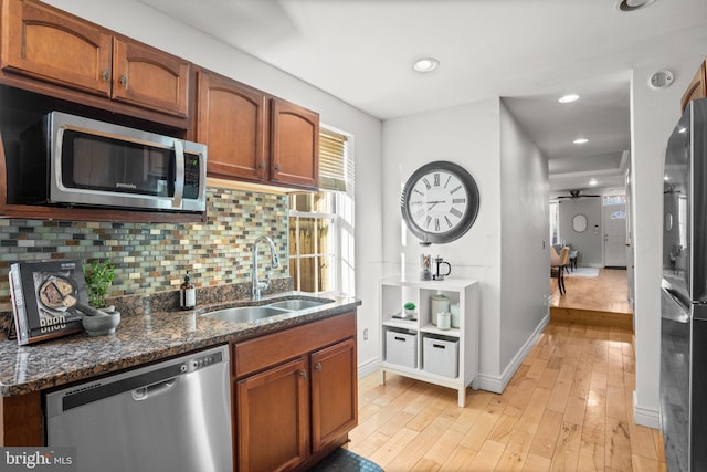 kitchen with stainless steel appliances, light wood-type flooring, backsplash, dark stone counters, and sink