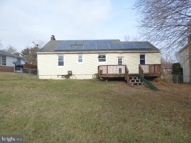 back of property with a lawn, a deck, and solar panels