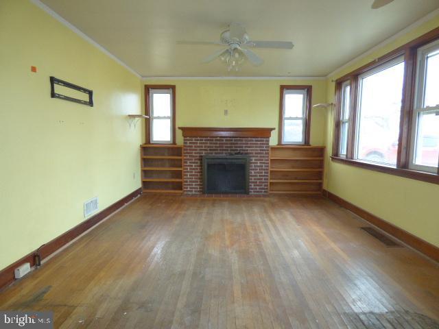 unfurnished living room with wood-type flooring, a brick fireplace, ceiling fan, and crown molding