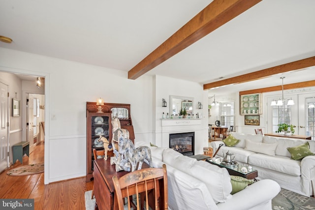 living room with beam ceiling, light hardwood / wood-style floors, and an inviting chandelier