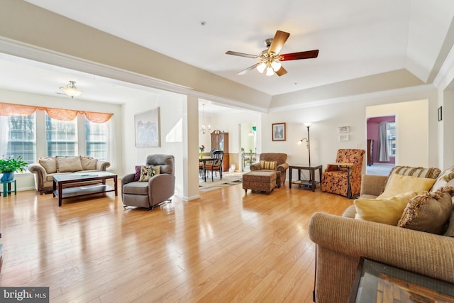 living room with ceiling fan with notable chandelier, a tray ceiling, and light hardwood / wood-style flooring