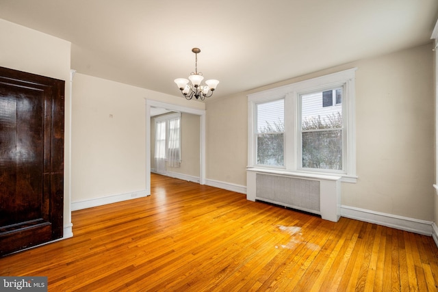 spare room with light hardwood / wood-style floors, radiator, and an inviting chandelier