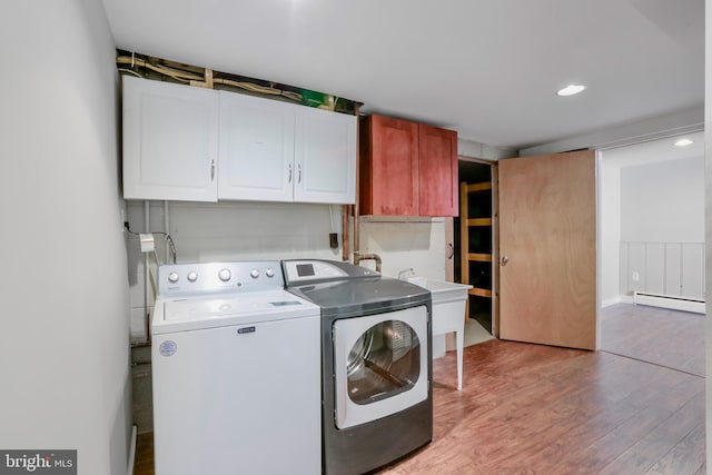 laundry area featuring washing machine and clothes dryer, sink, cabinets, a baseboard radiator, and light hardwood / wood-style floors