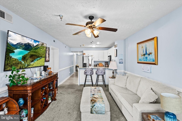 carpeted living room featuring ceiling fan and a textured ceiling