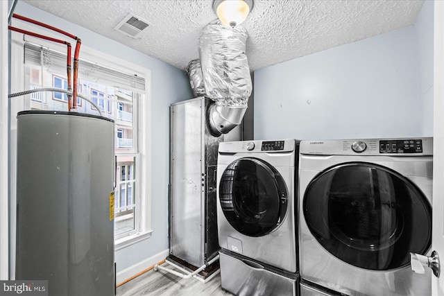 washroom with light wood-type flooring, independent washer and dryer, a textured ceiling, and water heater