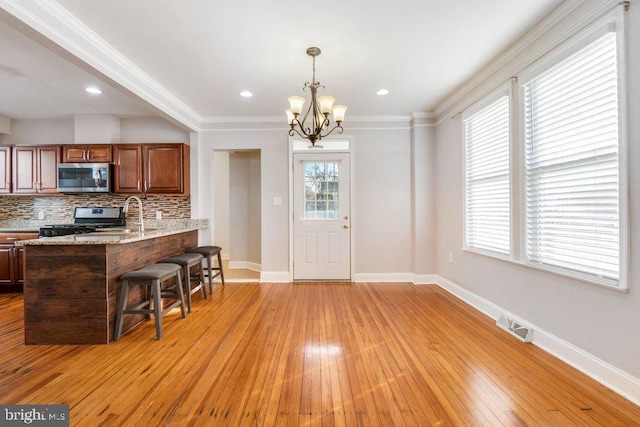 kitchen with tasteful backsplash, pendant lighting, an inviting chandelier, range, and a breakfast bar area