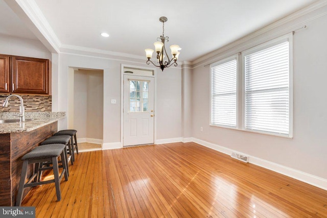 dining area with a notable chandelier, sink, light wood-type flooring, and ornamental molding