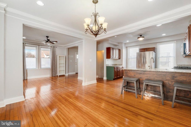 kitchen with ceiling fan with notable chandelier, crown molding, light stone countertops, and stainless steel appliances