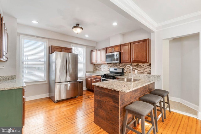 kitchen featuring a breakfast bar, backsplash, sink, light hardwood / wood-style flooring, and appliances with stainless steel finishes