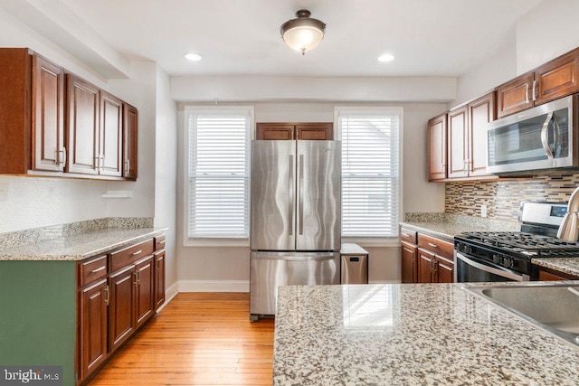 kitchen with light stone countertops, decorative backsplash, stainless steel appliances, and light hardwood / wood-style floors