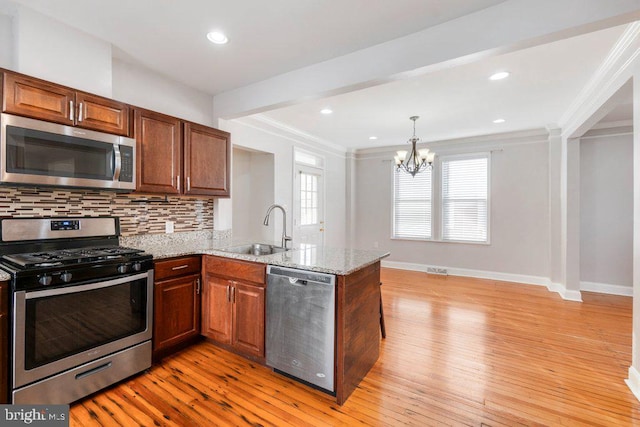 kitchen featuring sink, appliances with stainless steel finishes, light stone counters, kitchen peninsula, and a chandelier