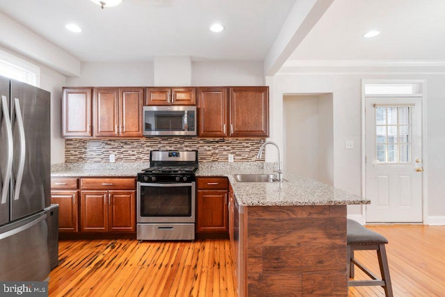 kitchen with decorative backsplash, light stone counters, stainless steel appliances, sink, and a breakfast bar area