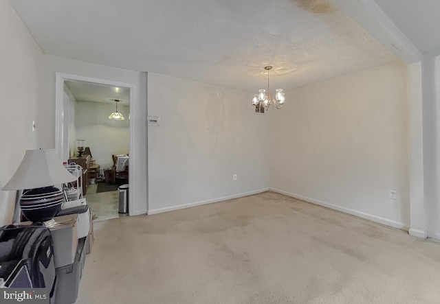 carpeted empty room featuring a chandelier and a textured ceiling