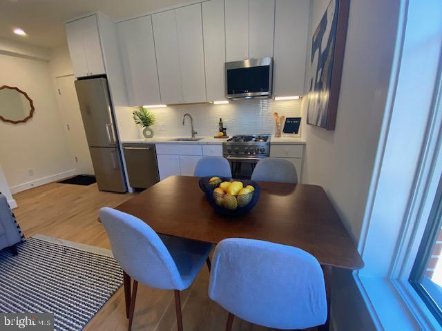 kitchen with appliances with stainless steel finishes, light wood-type flooring, sink, white cabinetry, and tasteful backsplash