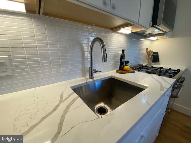 room details with stainless steel range with gas stovetop, gray cabinetry, light stone countertops, decorative backsplash, and sink