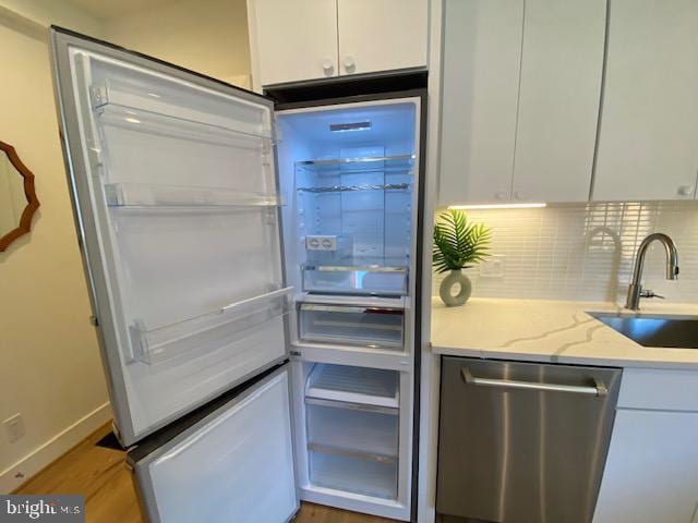 kitchen featuring stainless steel appliances, light stone counters, white cabinets, backsplash, and sink