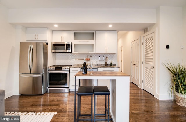 kitchen with stainless steel appliances, tasteful backsplash, dark hardwood / wood-style flooring, a breakfast bar area, and white cabinets