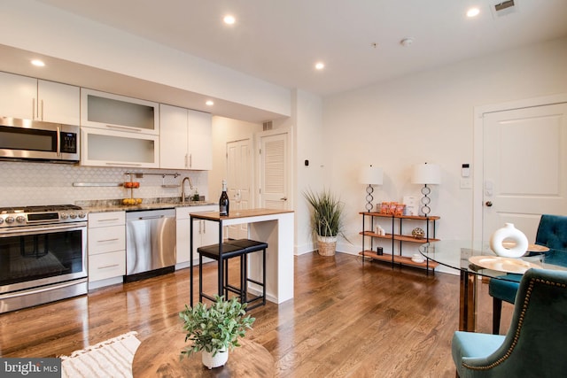 kitchen with decorative backsplash, appliances with stainless steel finishes, light stone counters, hardwood / wood-style flooring, and white cabinetry