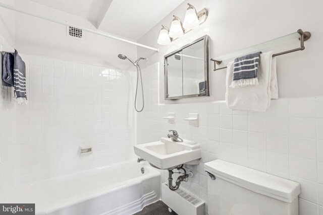 bathroom featuring tiled shower / bath combo, toilet, and tile walls