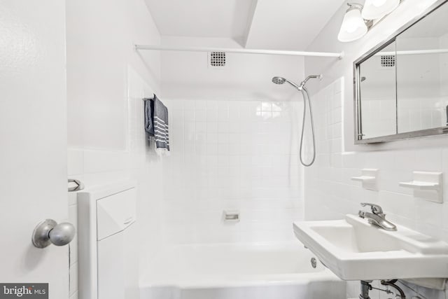 bathroom with tiled shower / bath combo, tasteful backsplash, sink, and tile walls