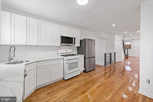 kitchen with light stone countertops, sink, decorative backsplash, white cabinets, and appliances with stainless steel finishes