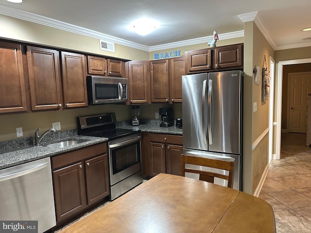 kitchen featuring dark stone counters, ornamental molding, stainless steel appliances, sink, and light tile patterned floors