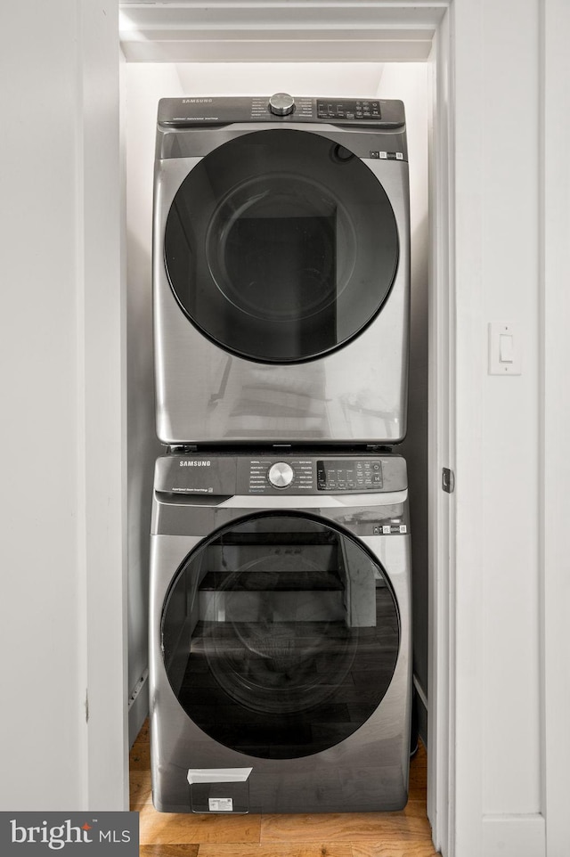 washroom with hardwood / wood-style flooring and stacked washing maching and dryer