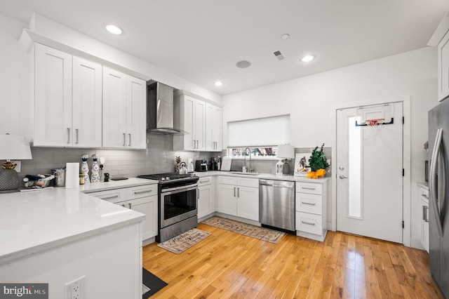 kitchen with sink, stainless steel appliances, wall chimney range hood, tasteful backsplash, and white cabinets