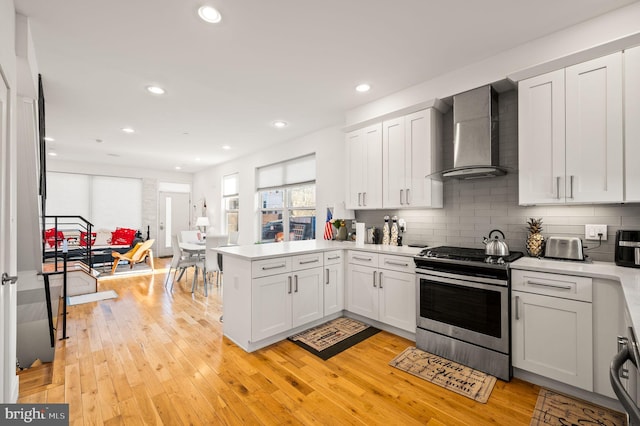 kitchen with white cabinets, wall chimney exhaust hood, kitchen peninsula, and stainless steel stove