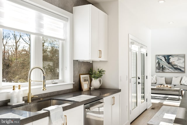 kitchen featuring light hardwood / wood-style floors, white cabinetry, stainless steel dishwasher, and sink