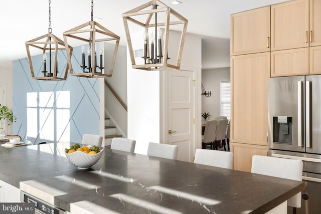 kitchen with hanging light fixtures, stainless steel refrigerator with ice dispenser, a notable chandelier, a kitchen bar, and light brown cabinetry