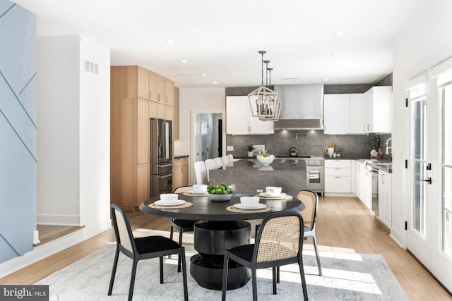 kitchen with decorative light fixtures, wall chimney exhaust hood, tasteful backsplash, premium appliances, and white cabinetry