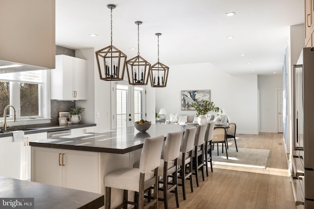 kitchen with pendant lighting, white cabinets, a kitchen breakfast bar, sink, and hardwood / wood-style flooring