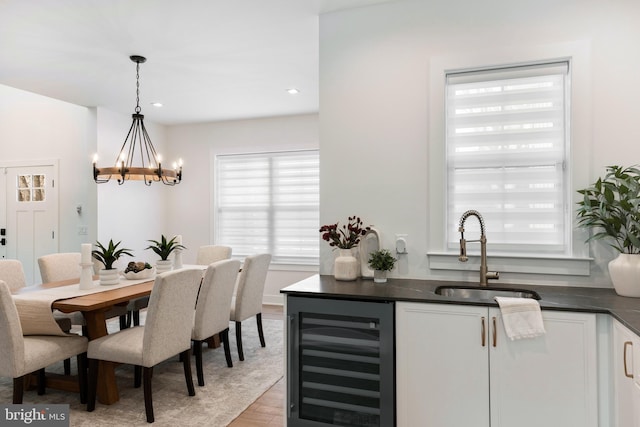 dining space with light hardwood / wood-style floors, sink, wine cooler, and a chandelier