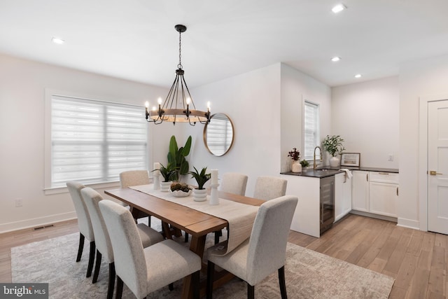 dining area with a chandelier, sink, beverage cooler, and light hardwood / wood-style flooring