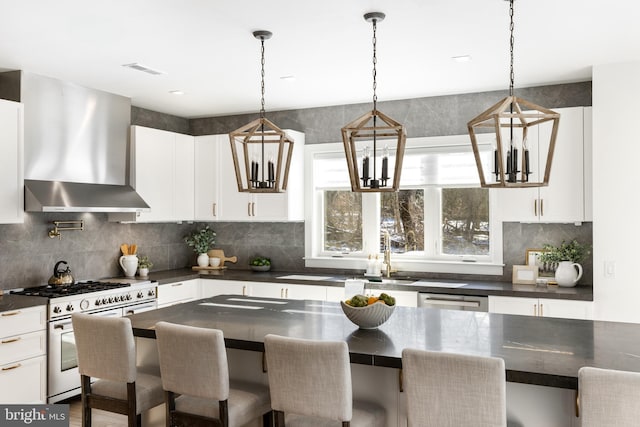 kitchen featuring wall chimney range hood, a breakfast bar area, decorative backsplash, white cabinets, and appliances with stainless steel finishes