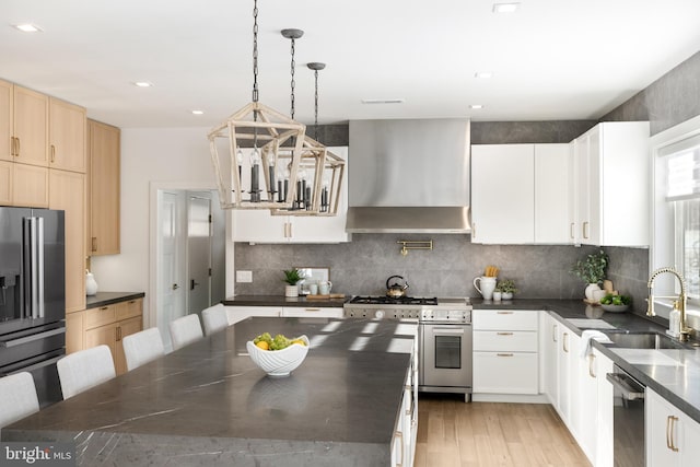 kitchen featuring sink, wall chimney exhaust hood, pendant lighting, white cabinets, and appliances with stainless steel finishes