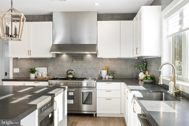 kitchen with white cabinets, decorative backsplash, wall chimney exhaust hood, and range with two ovens