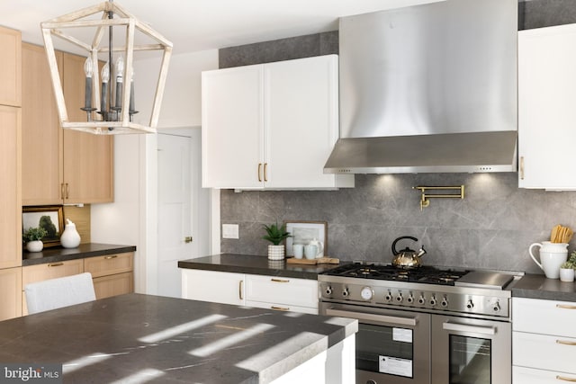 kitchen with backsplash, white cabinets, wall chimney range hood, hanging light fixtures, and stainless steel stove