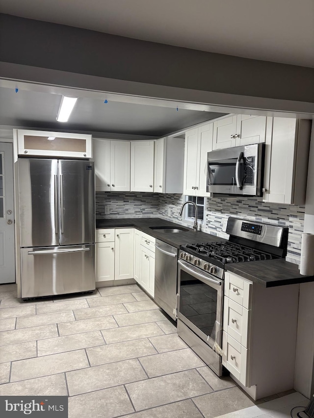 kitchen with stainless steel appliances, a sink, white cabinets, backsplash, and dark countertops