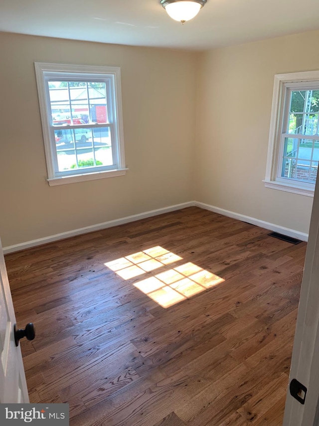 spare room with wood finished floors, visible vents, and baseboards