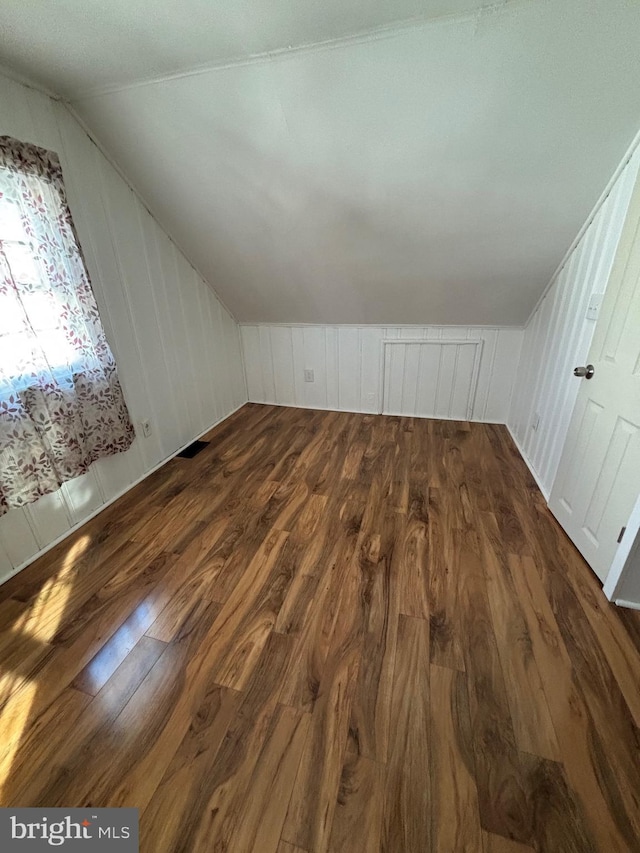 additional living space featuring visible vents, vaulted ceiling, and dark wood-type flooring